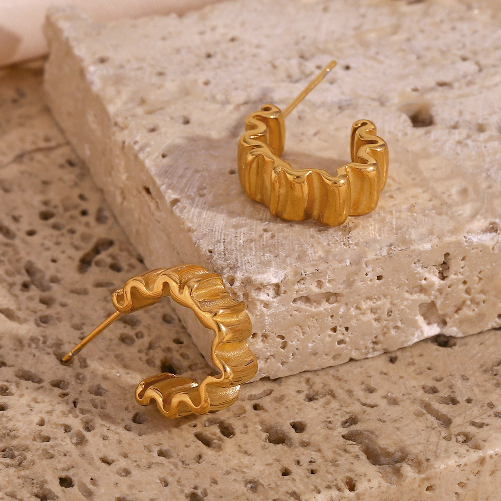 Folded gold tone earrings on textured stone