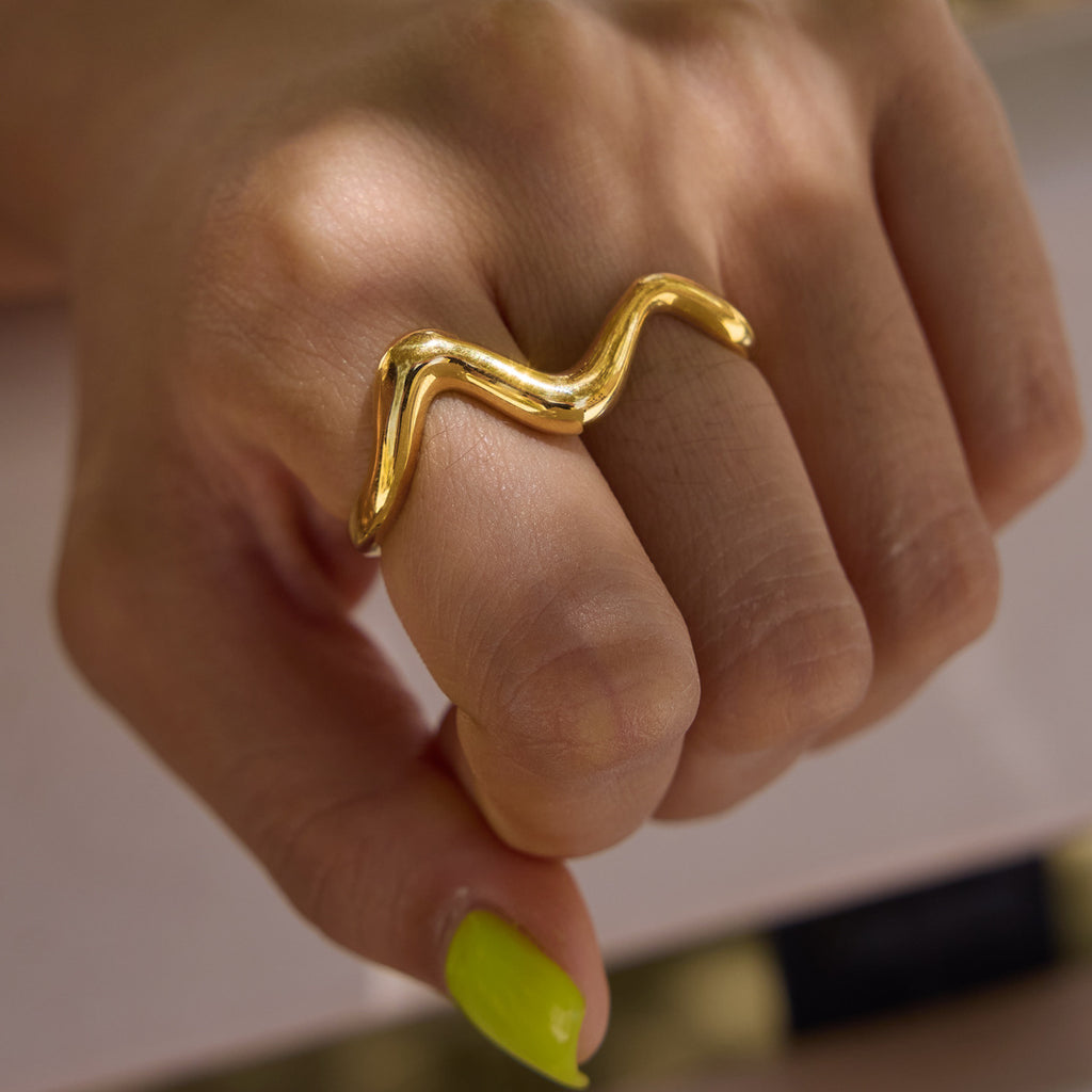 Close-up of gold tone wave spanning two fingers