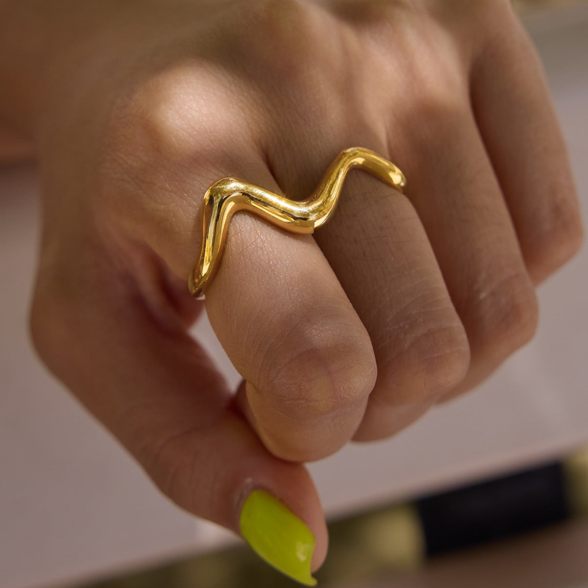 Close-up of gold tone wave spanning two fingers