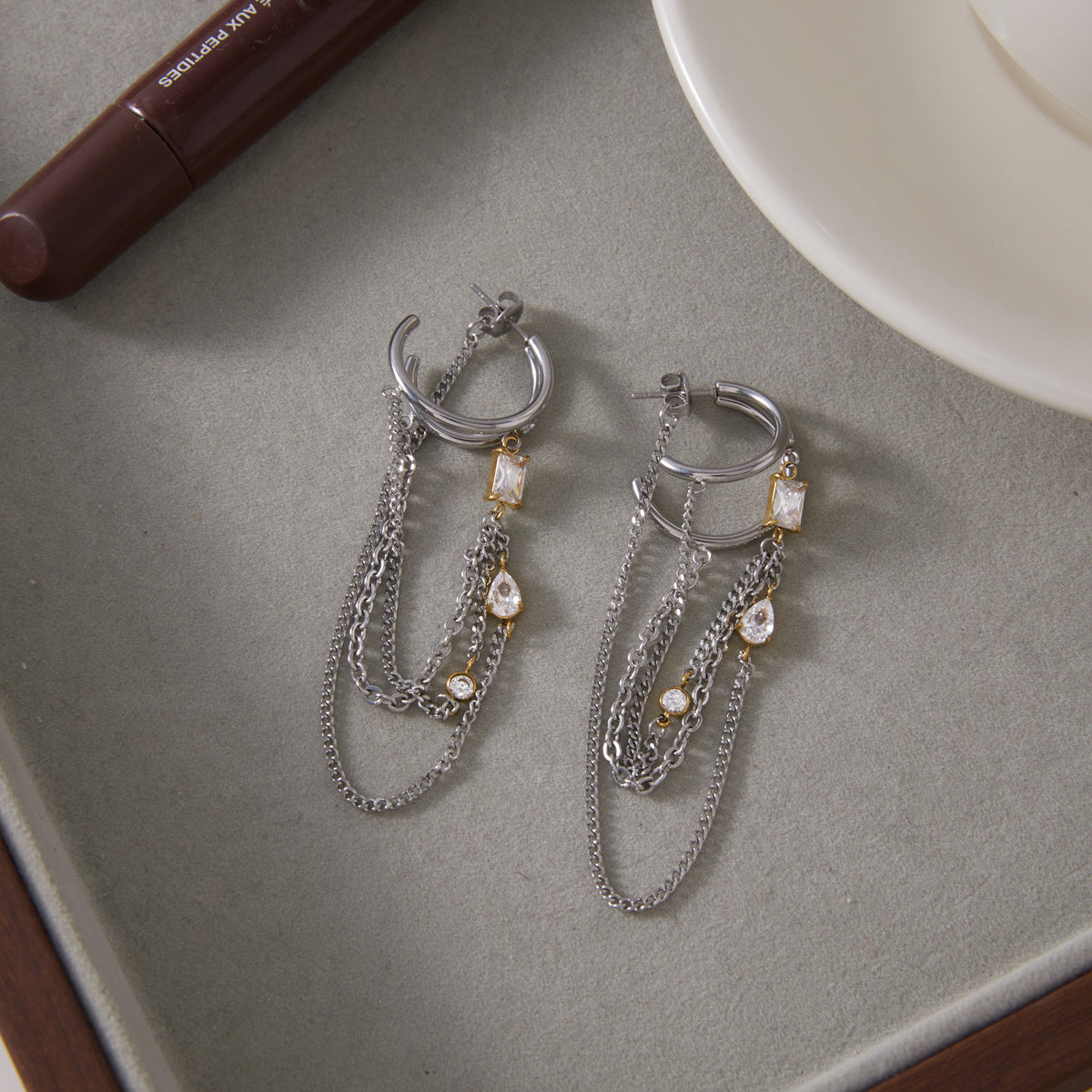 Pair of open hoop earrings with hanging chains on a tray
