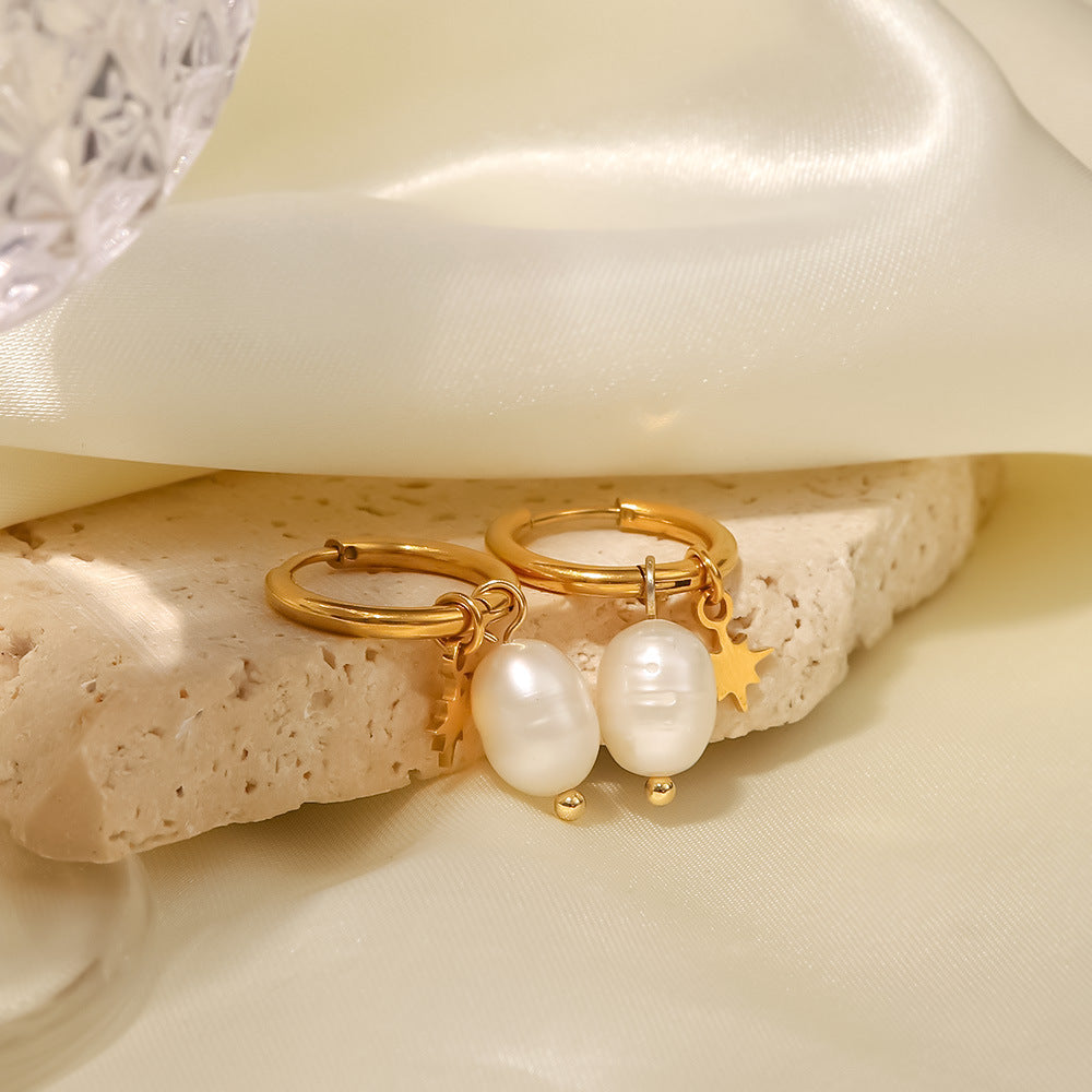 Pearl and star stainless steel hoop earrings resting beside fabric