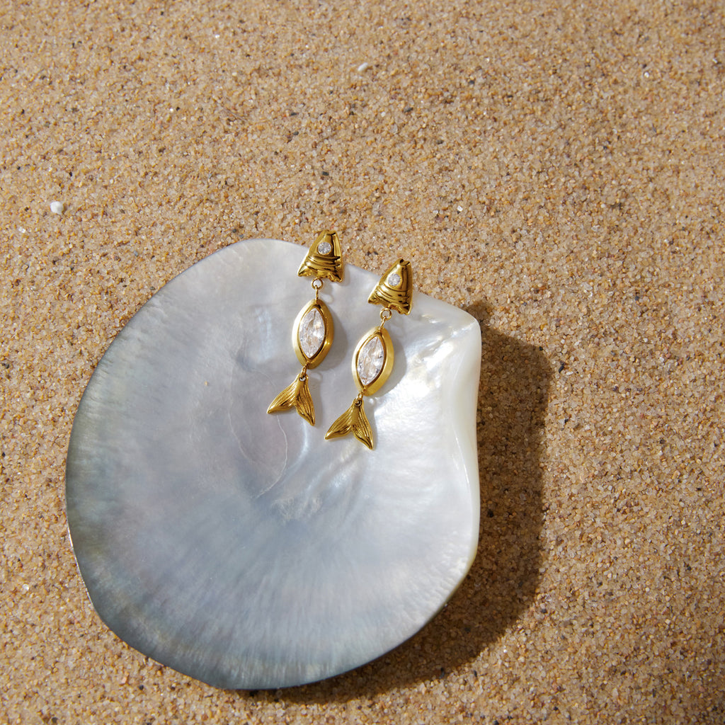 Pair of fish earrings displayed on a pale shell