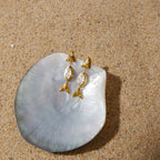 Pair of fish earrings displayed on a pale shell