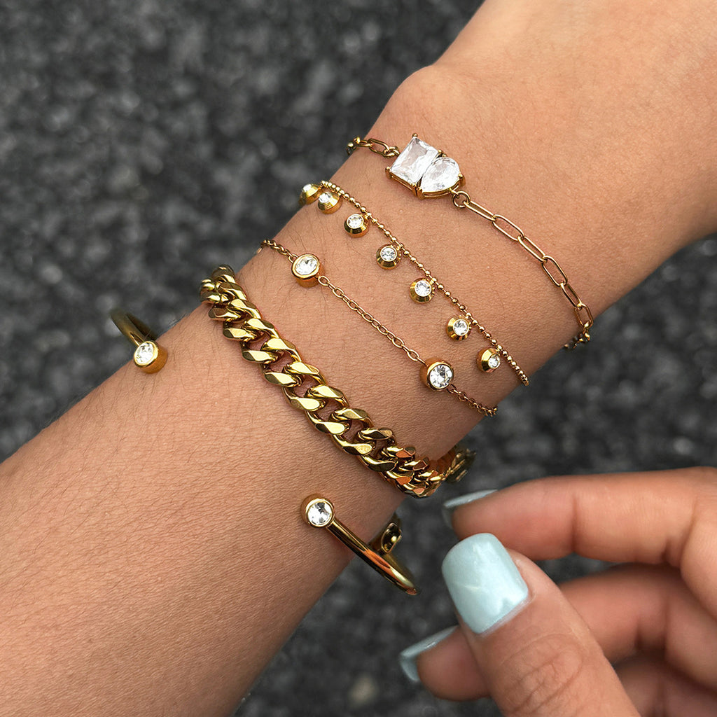 Gold-tone clear-stone bracelets and cuff stacked on a wrist