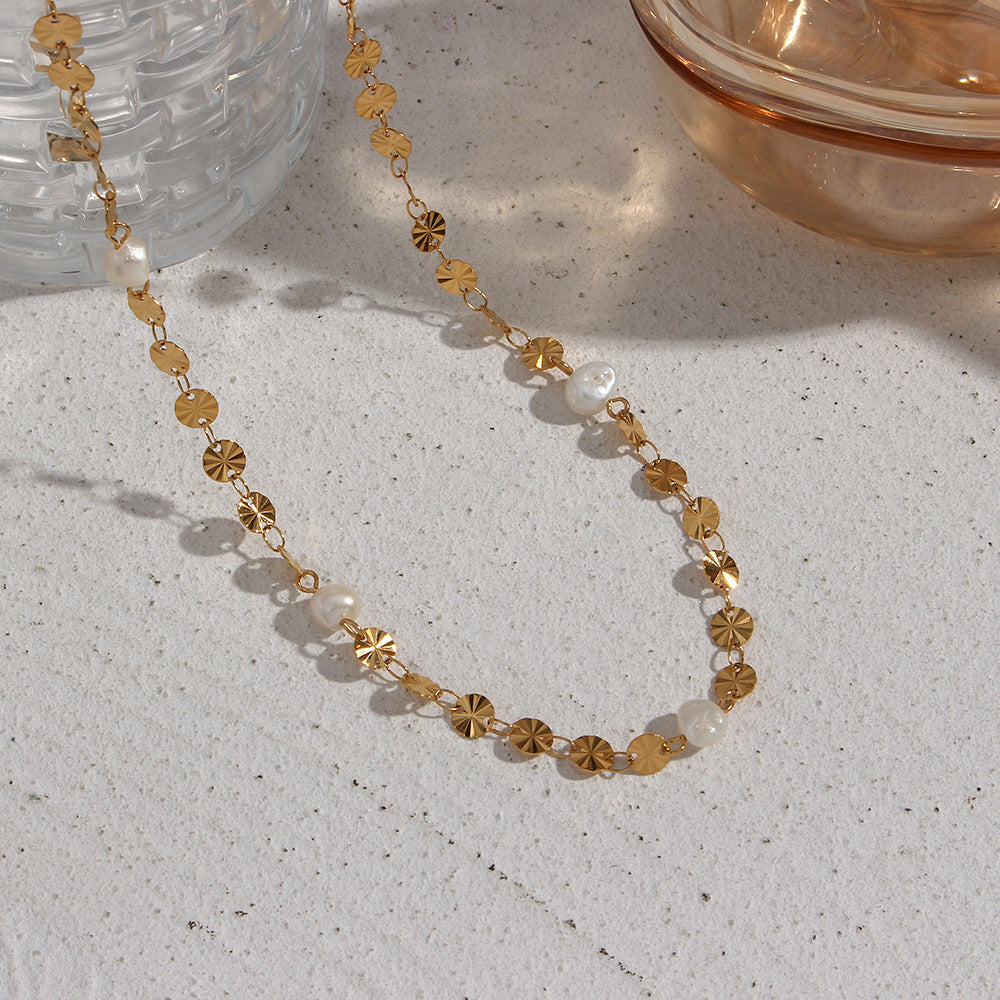 Gold-tone disc and pearl necklace arranged on a textured surface
