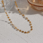 Gold-tone disc and pearl necklace arranged on a textured surface