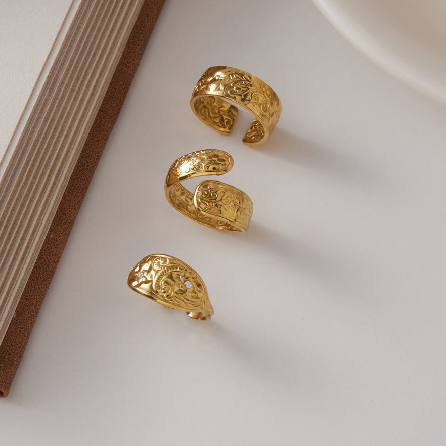 Three gold tone patterned rings displayed beside a book