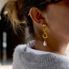 Model wearing gold-tone infinity drop earrings with white bead
