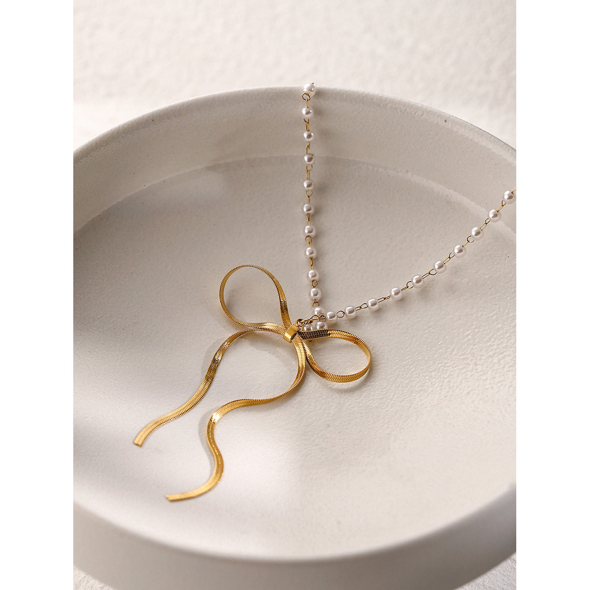 Gold plated bow pendant resting in a white dish