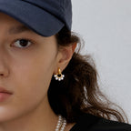 White resin pearl drop earrings worn with a cap