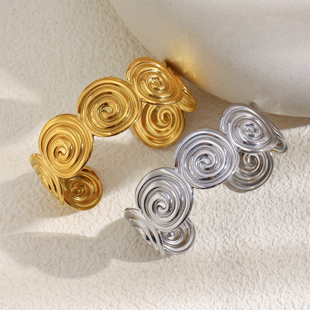 Gold plated and silver-color spiral disc cuffs on a textured display
