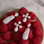 Pearl-look cross and elongated drop earrings beside raspberries