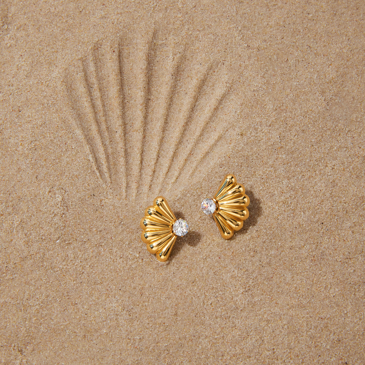 Gold finish fan earrings arranged on sand