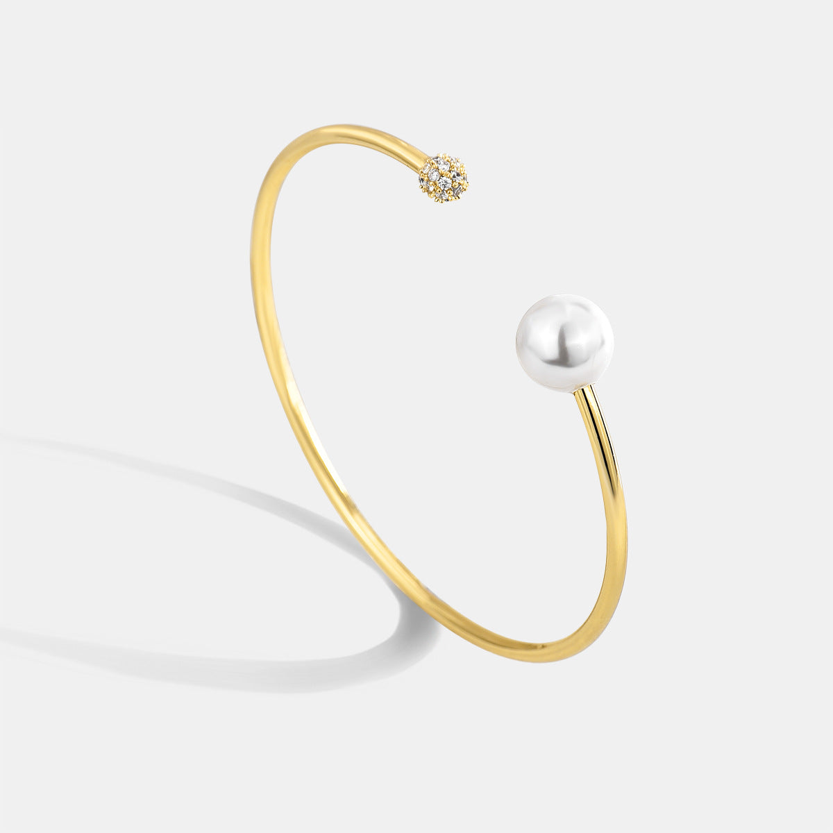 gold plated open bangle with pearl-style bead and clear stone cluster