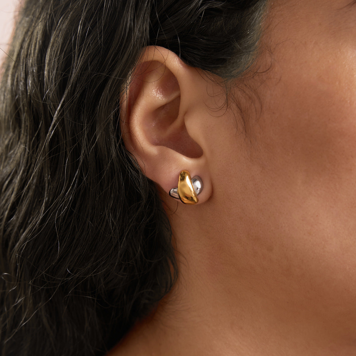 Two-tone crossed curve stud worn on an earlobe