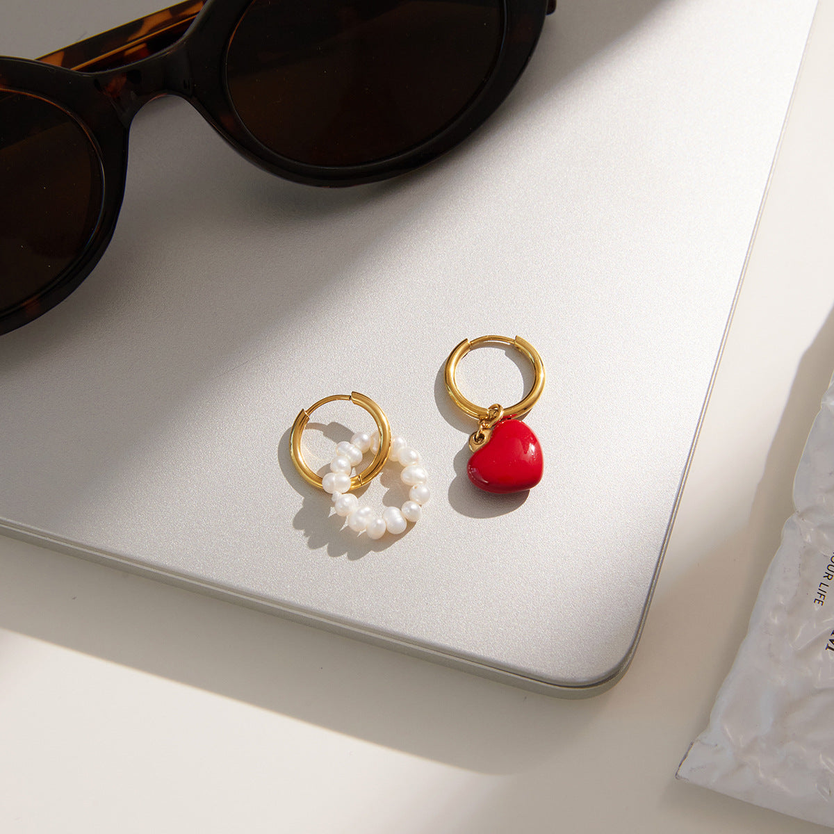 asymmetric heart and beaded huggie earrings styled on a desk