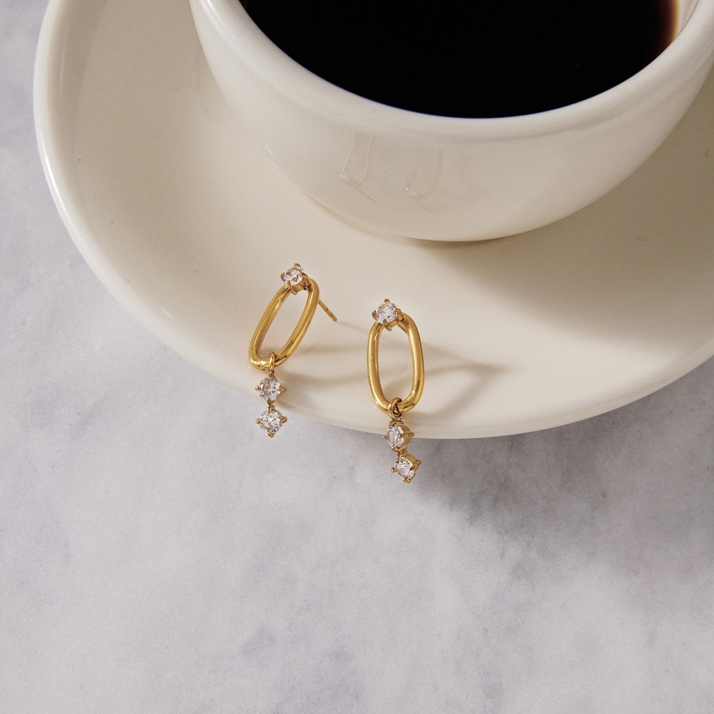 Clear stone drop earrings beside a cup