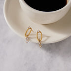 Clear stone drop earrings beside a cup