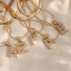 Layered gold-tone necklaces with imitation pearl letter pendants on fabric