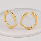 gold plated wavy oval hoop earrings on a white display