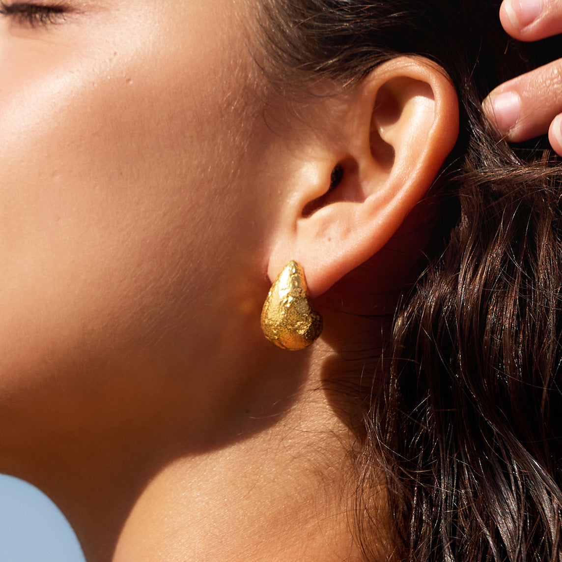 Textured gold-tone teardrop stud worn close-up