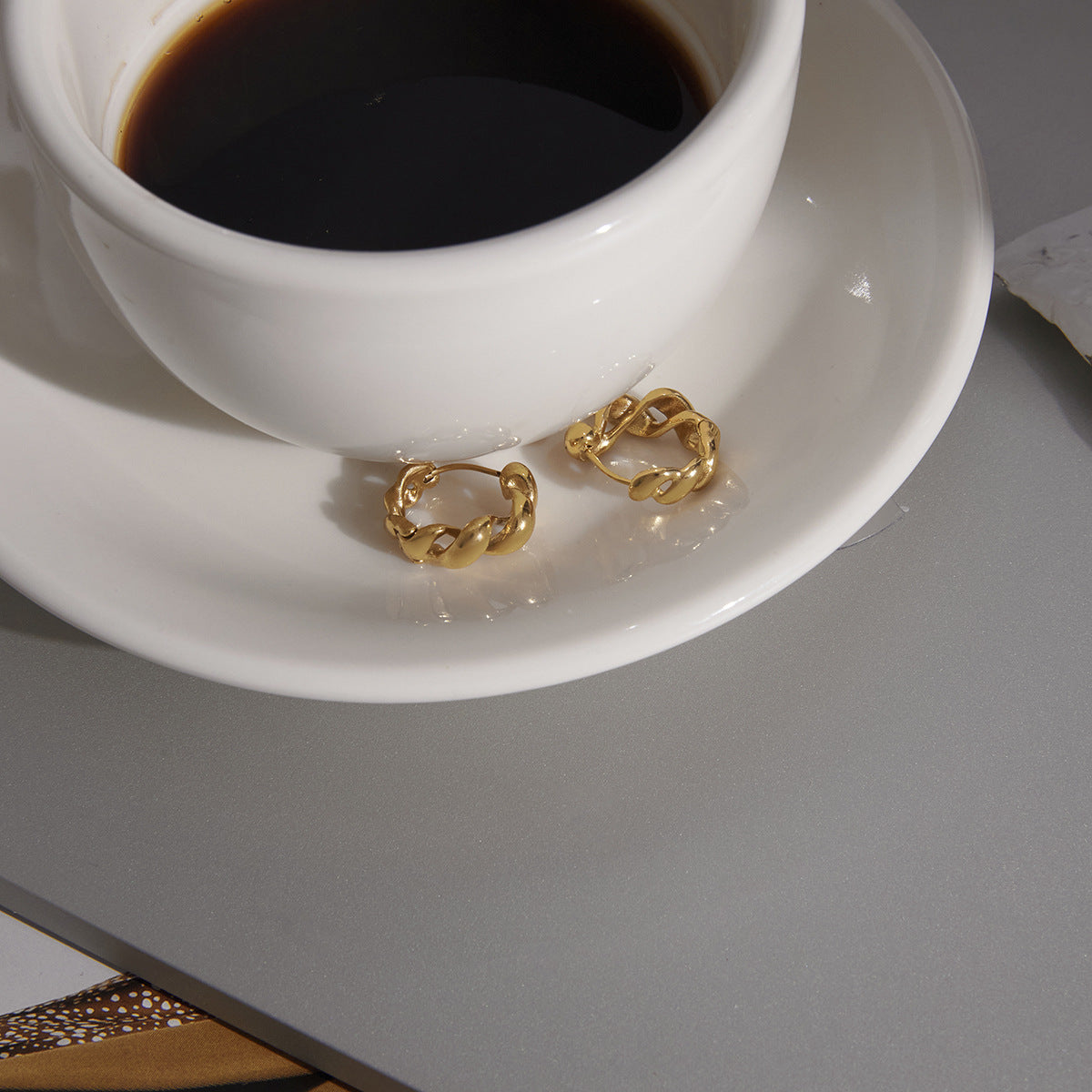 Pair of twisted link hoops displayed beside a cup