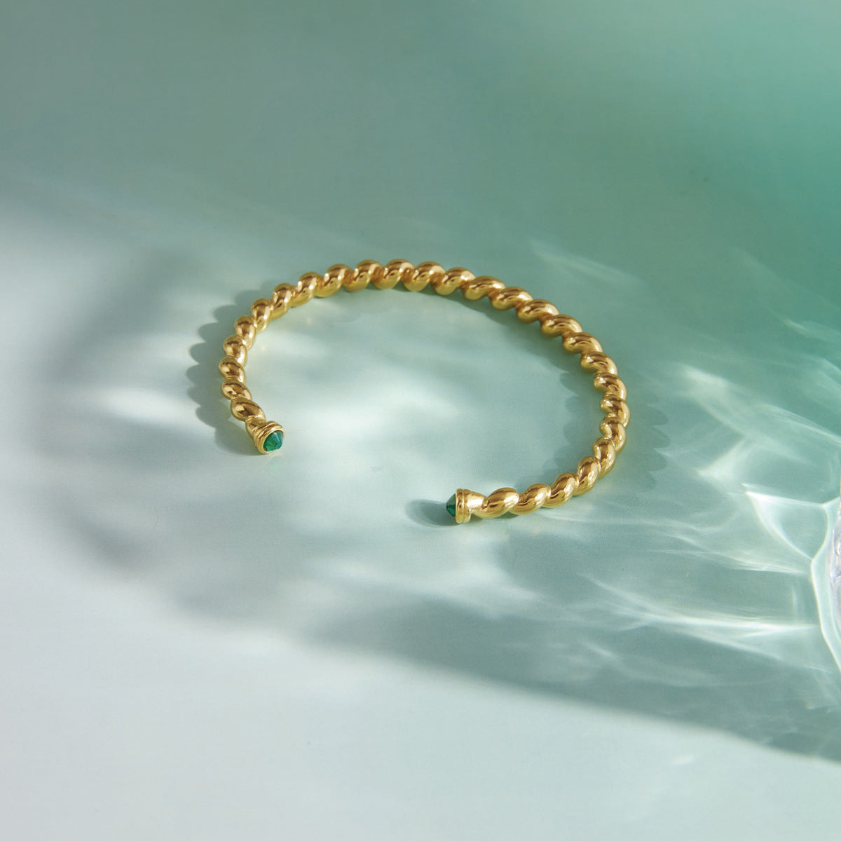 Gold tone rope-style cuff with green stones at the open ends
