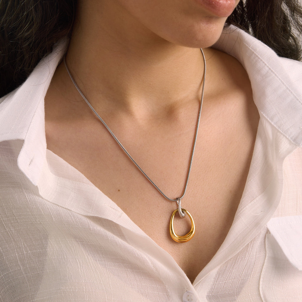 Open gold-tone teardrop necklace worn over a shirt