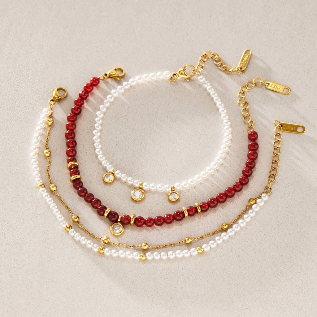 Three red and white beaded bracelet options arranged on stone