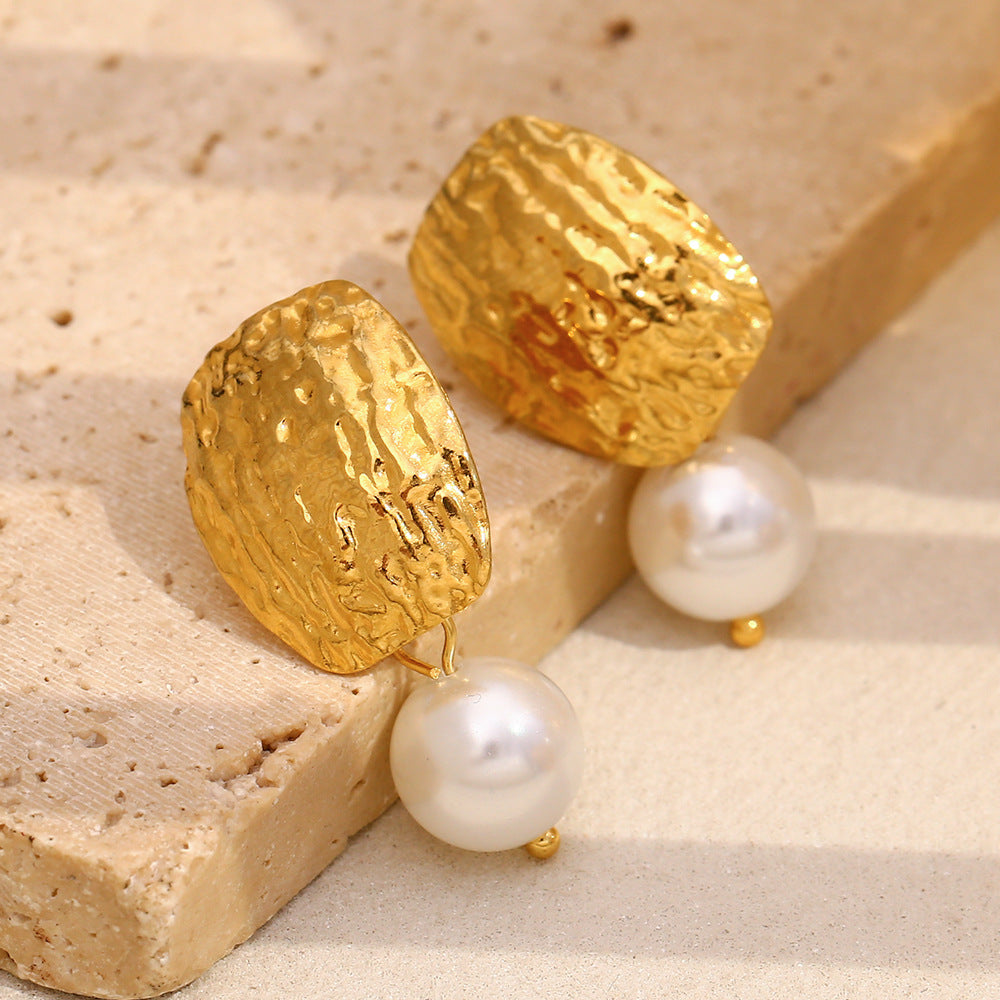 hammered gold and white pearl earrings on a beige stone block
