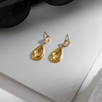 Gold tone teardrop earrings resting on a gray surface