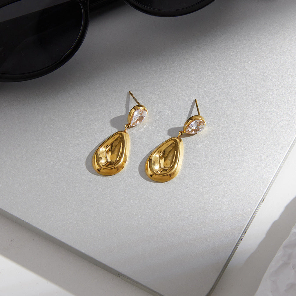 Gold tone teardrop earrings resting on a gray surface