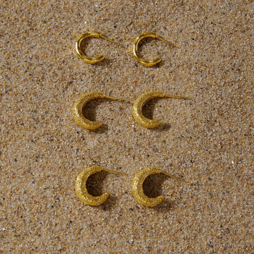 Three textured gold plated hoop designs on sand