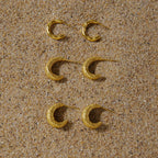 Three textured gold plated hoop designs on sand