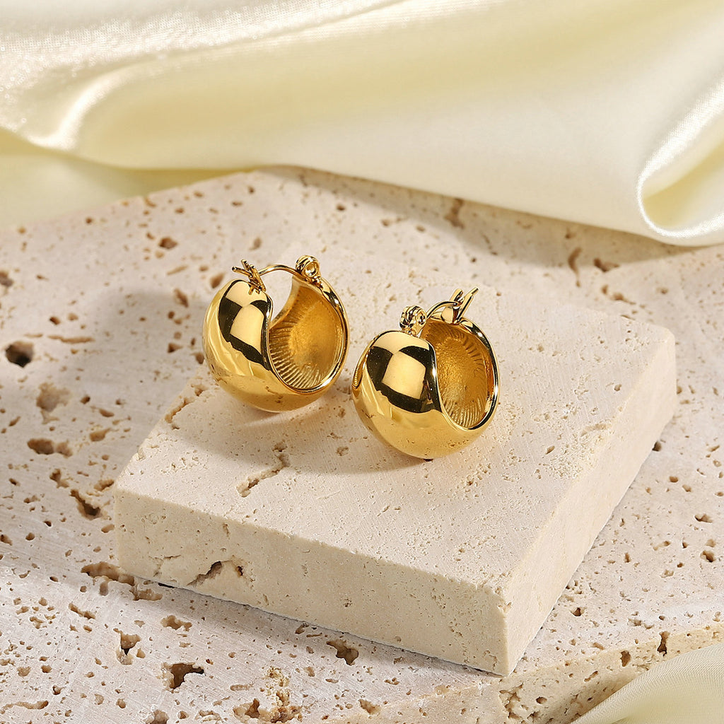 pair of polished dome huggie earrings displayed on pale stone