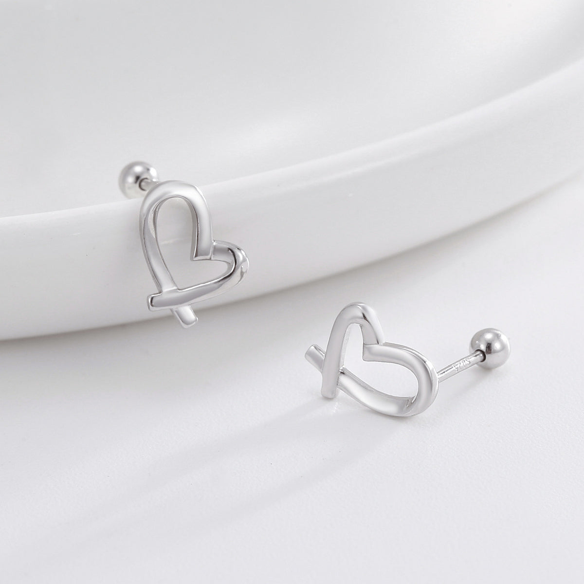 silver ribbon-heart earrings displayed on a curved white surface