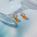 pair of amber-color resin drop hoops on blue reflective surface