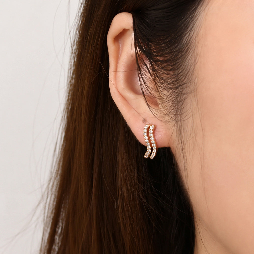 Gold tone wave huggie worn at the earlobe