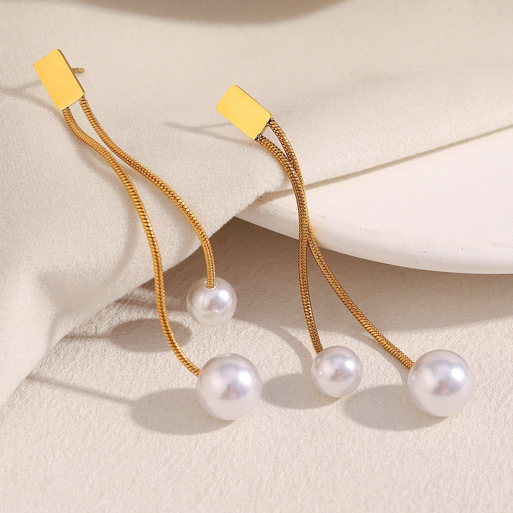 gold plated staggered pearl chain earrings laid on a cream surface