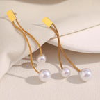 gold plated staggered pearl chain earrings laid on a cream surface