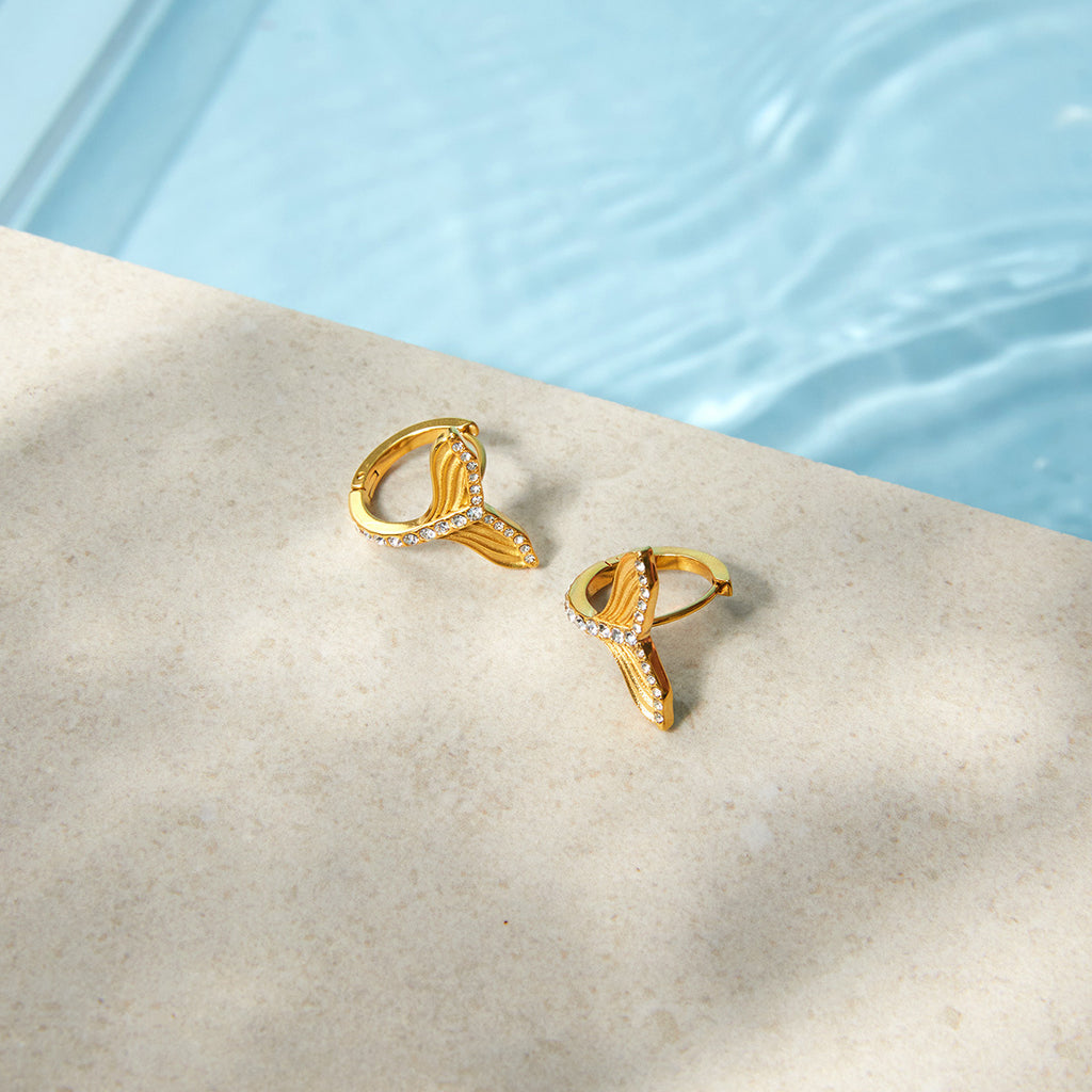 Gold-tone tail earrings beside a pool