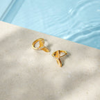 Gold-tone tail earrings beside a pool