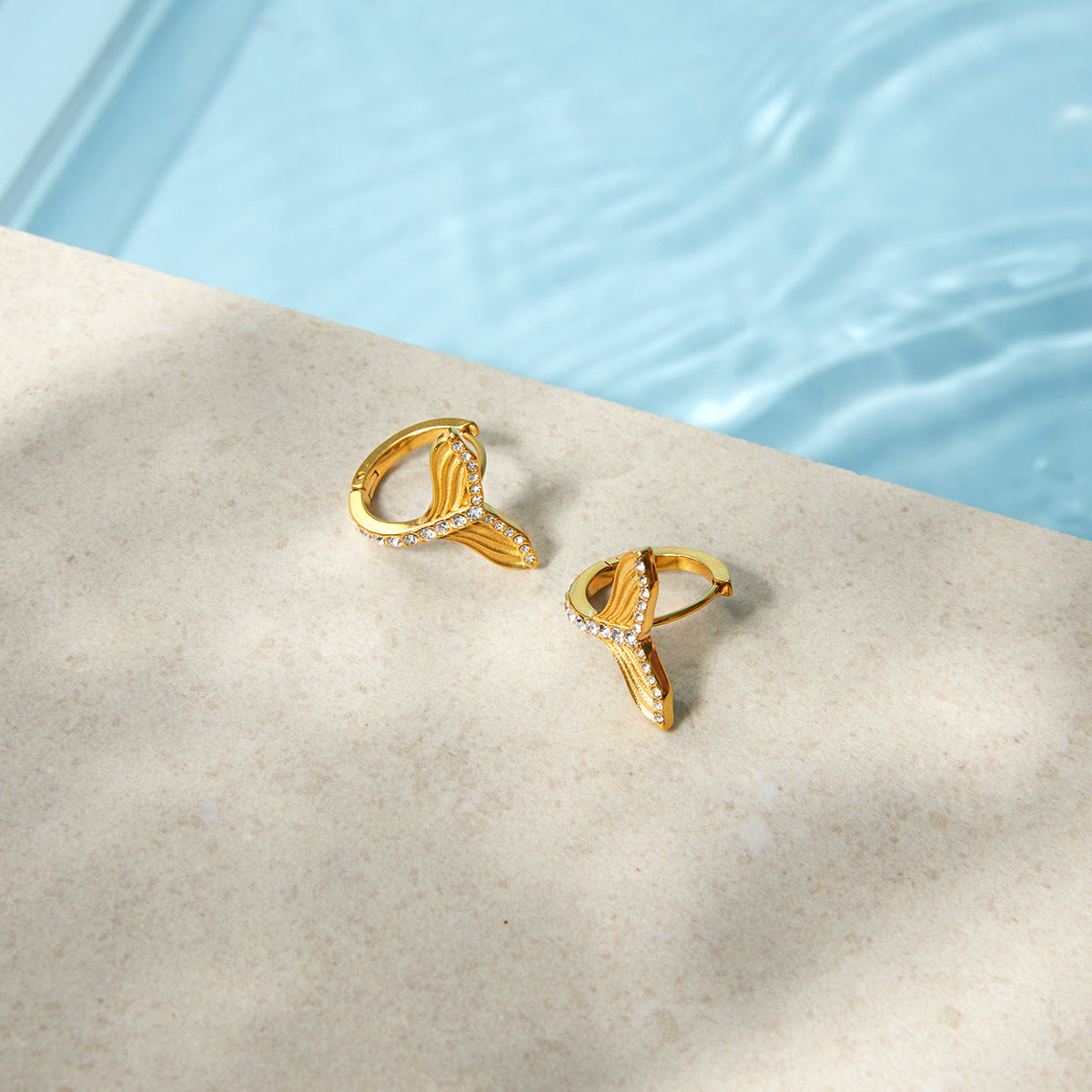 Gold-tone tail earrings beside a pool
