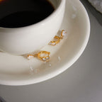 Gold-tone clear stone hoops beside a cup