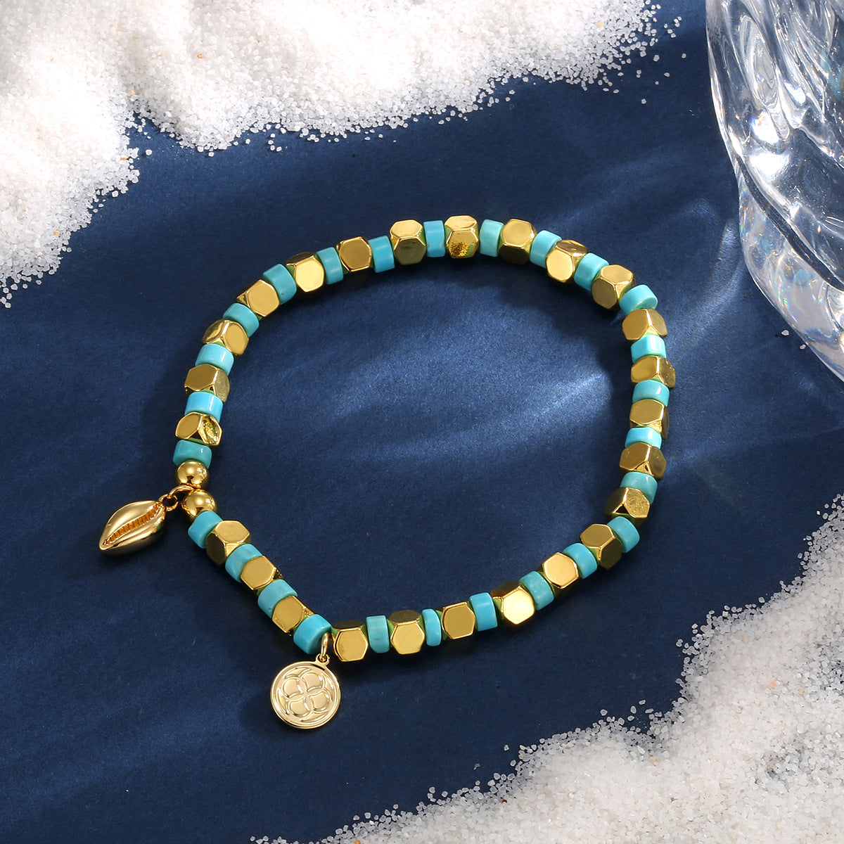 cowrie charm bracelet styled on blue fabric with white granules