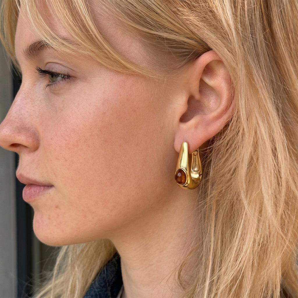 Brown resin accent U hoop earring worn on an ear