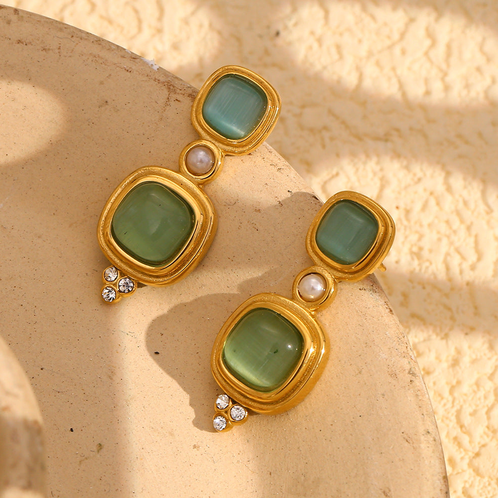 gold and green geometric drop earrings on a neutral pedestal