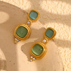 gold and green geometric drop earrings on a neutral pedestal