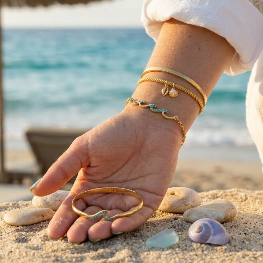 Blue wave accent bracelet layered with gold tone bangles at the beach