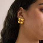 Gold tone woven square stud earring worn on an ear